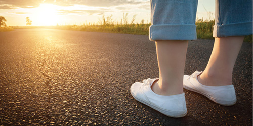 Woman's feet facing the sun along a road