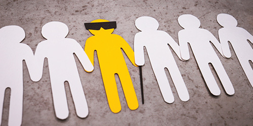 Paper cut outs of people with a yellow one in the middle with eyeglasses and cane